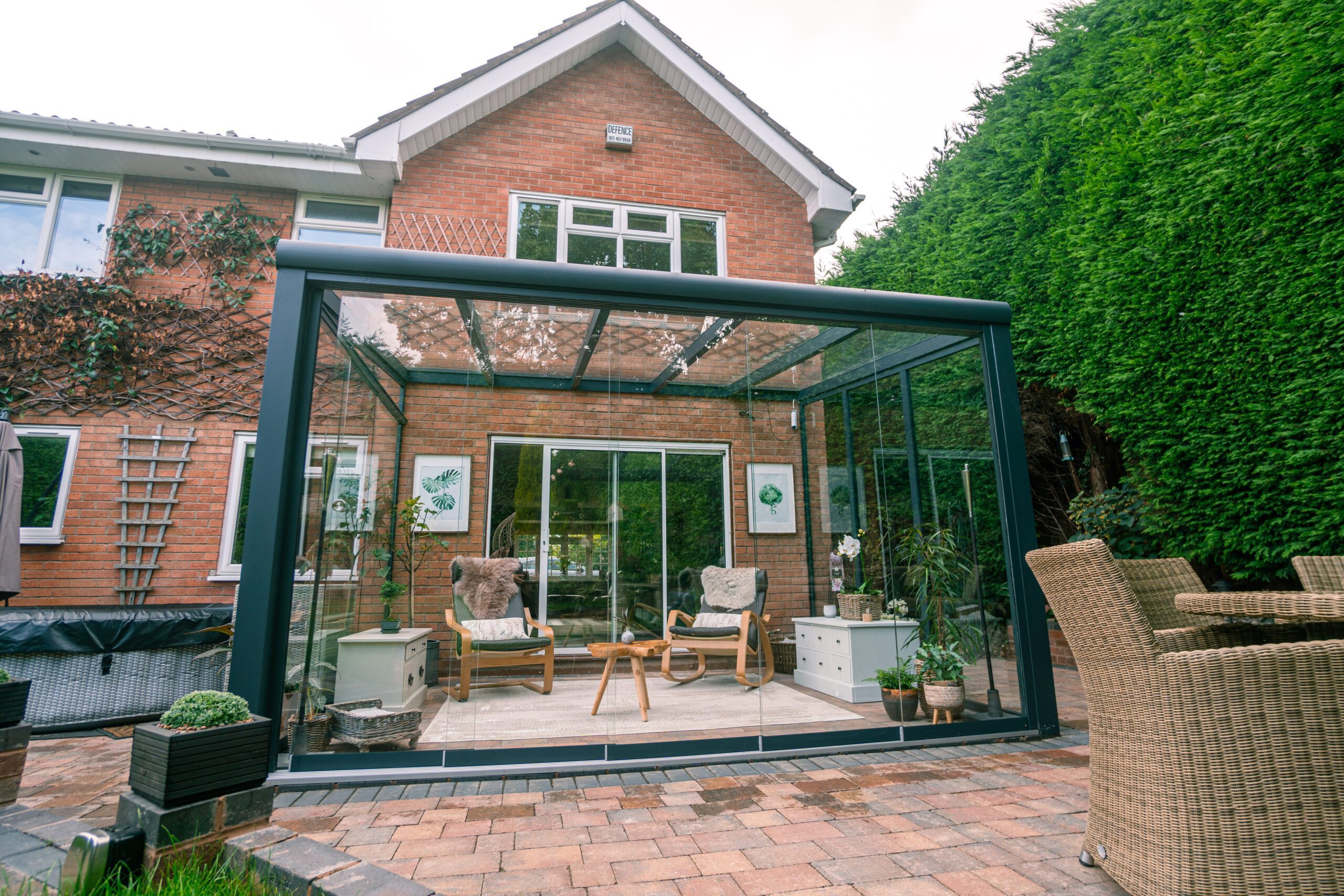 A modern glass veranda attached to the rear of a brick house with chairs inside